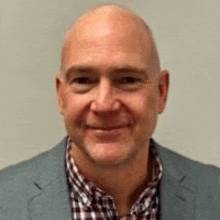 a bald man wearing a suit and a plaid shirt is smiling for the camera .