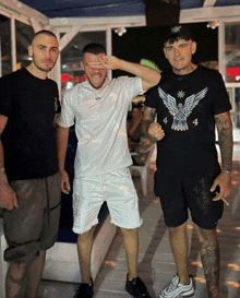 a man wearing a black shirt with an eagle on it stands with two other men