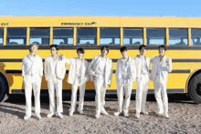 a group of young men in white suits are standing in front of a yellow school bus .