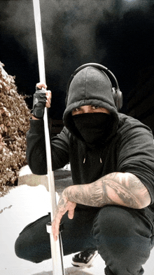 a man wearing headphones and a black hoodie holds a pole in front of his face