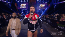 a wrestler speaking into a microphone in front of a aew sign