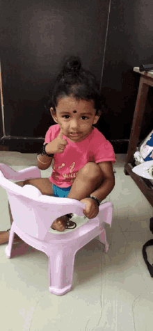 a little girl wearing a pink shirt that says girl power is sitting on a pink chair and giving a thumbs up