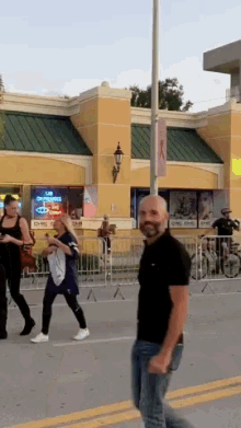 a man in a black shirt walks down a street in front of a building with a neon sign that says gmc on it