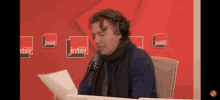 a man wearing headphones is reading a piece of paper in front of a red wall with inter written on it