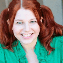 a woman with red hair and pigtails wearing a green shirt is smiling .