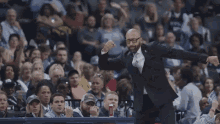 a man in a suit and glasses is standing in front of a crowd of people at a basketball game .