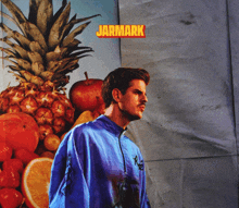 a man in a blue jacket stands in front of a pineapple and other fruits with the word jarmark above him