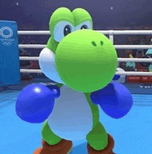 a green dinosaur is wearing blue boxing gloves and standing in a boxing ring .