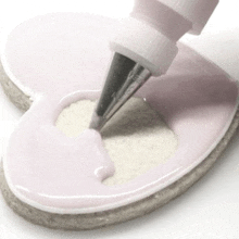 a heart shaped cookie is being decorated with frosting and a piping nozzle .