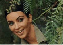 a close up of kim kardashian smiling behind a tree