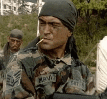 a man in a military uniform is smoking a cigarette while wearing a bandana .