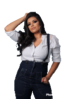 a woman wearing suspenders and a white shirt stands with her hand in her hair