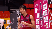 a basketball player drinks water from a bottle while standing in front of a sign that says " zaragoza "