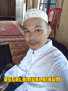 a man wearing a white hat is sitting in front of a red chair with the words assalamualaikum written above him