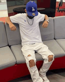 a man is sitting on a couch wearing a blue hat and a white shirt .