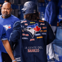 a blue jays player wears a jacket that says " la gente del barrio " on the back