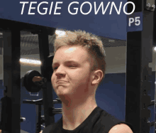 a young man stands in front of a sign that says tegie gowno