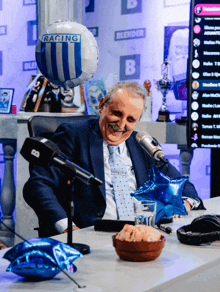 a man sitting in front of a microphone with a racing balloon behind him