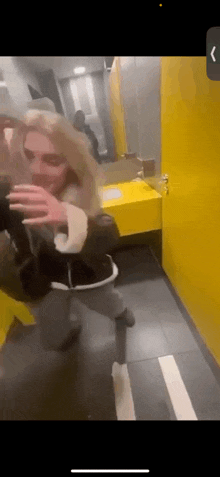 a woman is taking a selfie in a public restroom with a yellow sink .