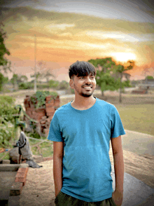 a young man wearing a blue shirt is smiling in front of a sunset