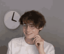 a young man wearing glasses and a white shirt is smiling in front of a clock .