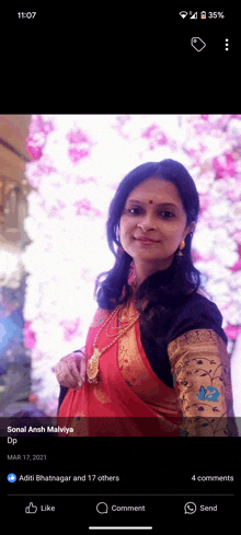 a woman in a red and gold dress is standing in front of a wall of pink flowers ..