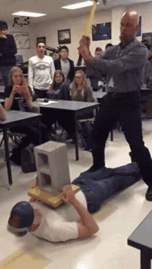 a man is laying on the floor with a brick on his head while another man swings a baseball bat at him