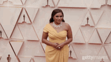 a woman wearing a yellow dress and a diamond necklace is standing in front of a wall with oscar statues