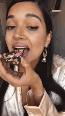 a woman with a nose ring is eating a piece of chocolate cake