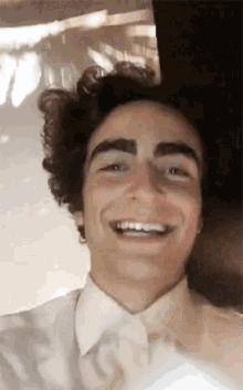 a young man with curly hair and eyebrows is smiling and looking at the camera .