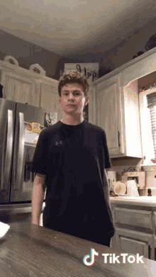 a young man in a black shirt is standing in a kitchen with a sign that says hope on it