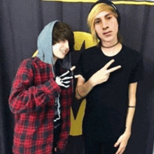 a boy in a plaid shirt and a boy in a black shirt are standing next to each other and making peace signs .