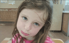 a little girl with long brown hair and blue eyes looks at the camera