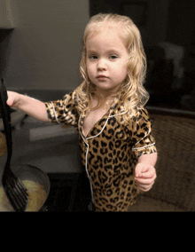 a little girl in a leopard print shirt is holding a black fork