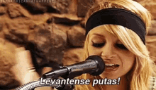 a woman is singing into a microphone while wearing a headband and saying levantense putas !