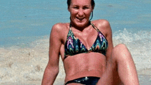 a woman in a bikini is sitting on the beach in the water .