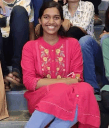 a woman in a pink dress is sitting on a set of stairs with her legs crossed and smiling .