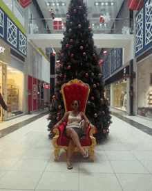 a woman sits in a chair in front of a christmas tree in a shopping mall