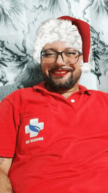 a man wearing glasses and a santa hat has a red shirt with a white cross on it