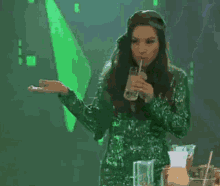 a woman in a green sequined dress is drinking from a glass through a straw