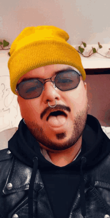 a man wearing a yellow beanie and sunglasses sticks his tongue out