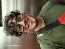 a man with curly hair wearing glasses and a green shirt is smiling