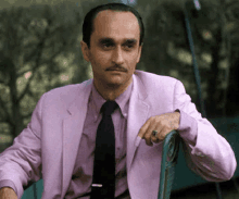 a man in a pink suit and black tie is sitting on a chair .