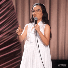 a woman in a white dress is holding a microphone in front of a curtain that says netflix on it