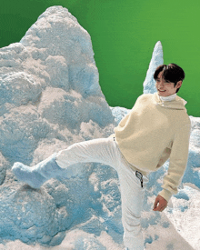 a man wearing a white sweater and white pants stands in front of a snowy mountain