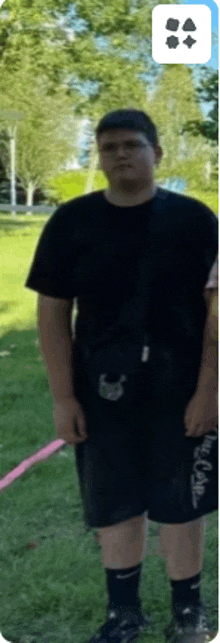 a man in a black shirt and black shorts is standing in a park .