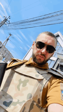 a man wearing sunglasses and a camo vest takes a picture of himself