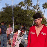 a man wearing a red bape hoodie and a black hat is standing in front of a crowd of people .