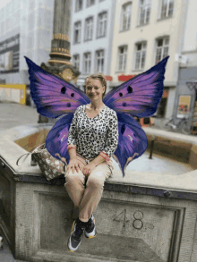 a woman with purple butterfly wings sits on a stone wall