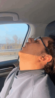 a young man wearing glasses is sleeping in a car